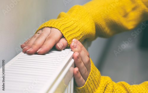 The woman warms her hands on the radiator