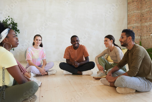 Multiethnic group of people sitting on the floor and discussing something with each other