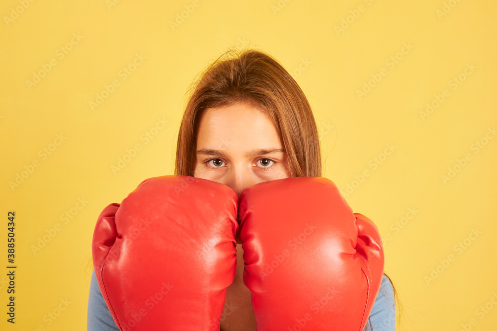 Portrait of young fighter woman wearing red boxing gloves on yellow background Portrait of young fighter woman wearing red boxing gloves on yellow background