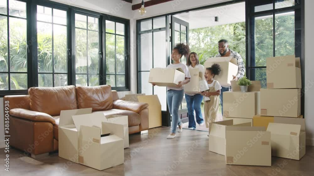 Happy African American young family bought new house. Mom, Dad, and child smiling happy hold cardboard boxes for move object walking into big modern home. New real estate dwelling, loan and mortgage.