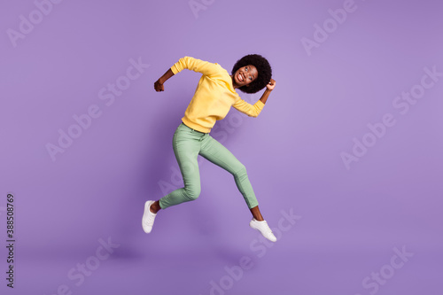 Full size photo of excited dark skin girl jump grimacing wear yellow pullover isolated over purple color background