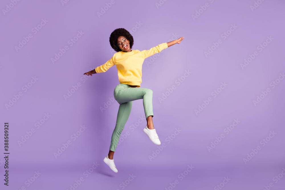 Full size photo of excited dark skin girl jump up wear yellow sweater green pants isolated on purple color background