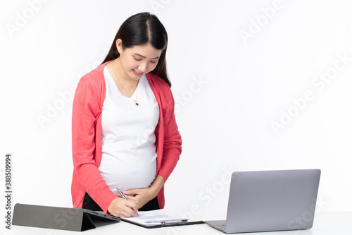 Cheerful pregnant businesswoman writing on document standing at her working place in office on white background. Pregnant woman working concept.