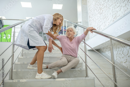 Blonde nurse helping the senior woman who fell down on the strairs photo