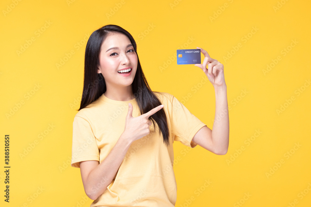 Cheerful young asian woman in yellow T-shirt holding bank card isolated on yellow background Cheerful young asian woman in yellow T-shirt holding bank card isolated on yellow background
