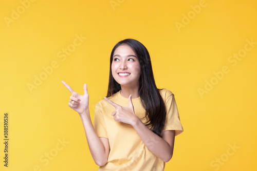 Beautiful woman wearing casual clothes smile and pointing finger at copy space on pastel yellow wall background studio portrait.