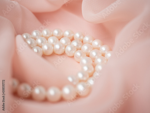 Women wedding jewelry. Necklace of natural pearls on pink gentle chiffon fabric as background. Luxury wedding background. Macro shot of wedding jewelry. Soft and delicate wavy pastel material
