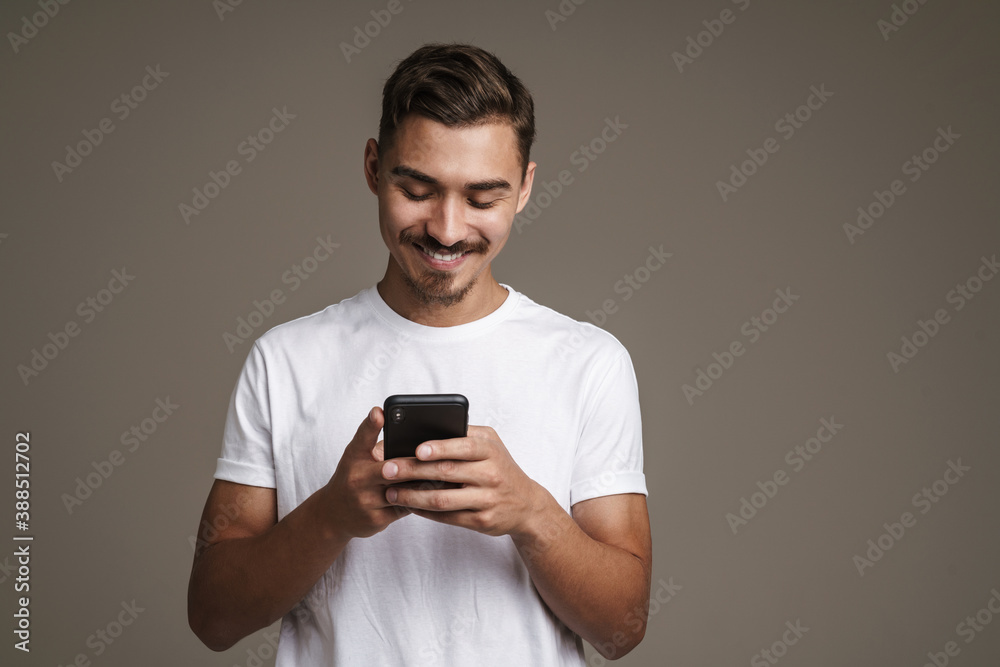 Image of joyful unshaven guy smiling and using cellphone Image of joyful unshaven guy smiling and using cellphone