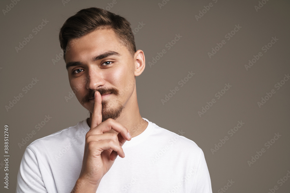Image of pleased unshaven guy showing silence gesture Image of pleased unshaven guy showing silence gesture
