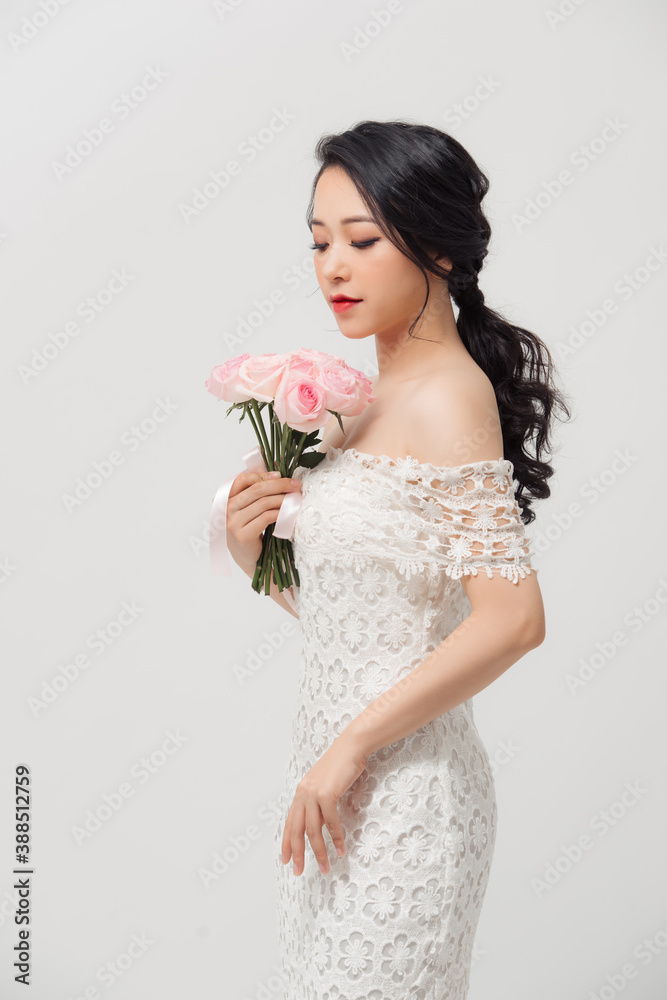 Young beautiful pretty Asian girl standing and holding pink roses over white background. Young beautiful pretty Asian girl standing and holding pink roses over white background.