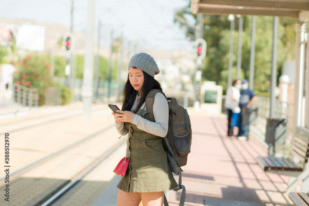 outdoors portrait of young happy and beautiful Asian Korean tourist woman with backpack using mobile phone on train station waiting excited in holidays travel and vacation outdoors portrait of young happy and beautiful Asian Korean tourist woman with backpack using mobile phone on train station waiting excited in holidays travel and vacation