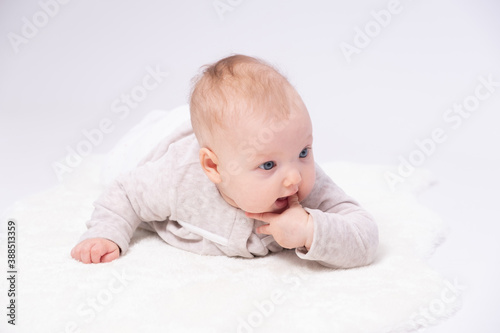 Charming baby is lying on the floor and sucking one’s small fingers