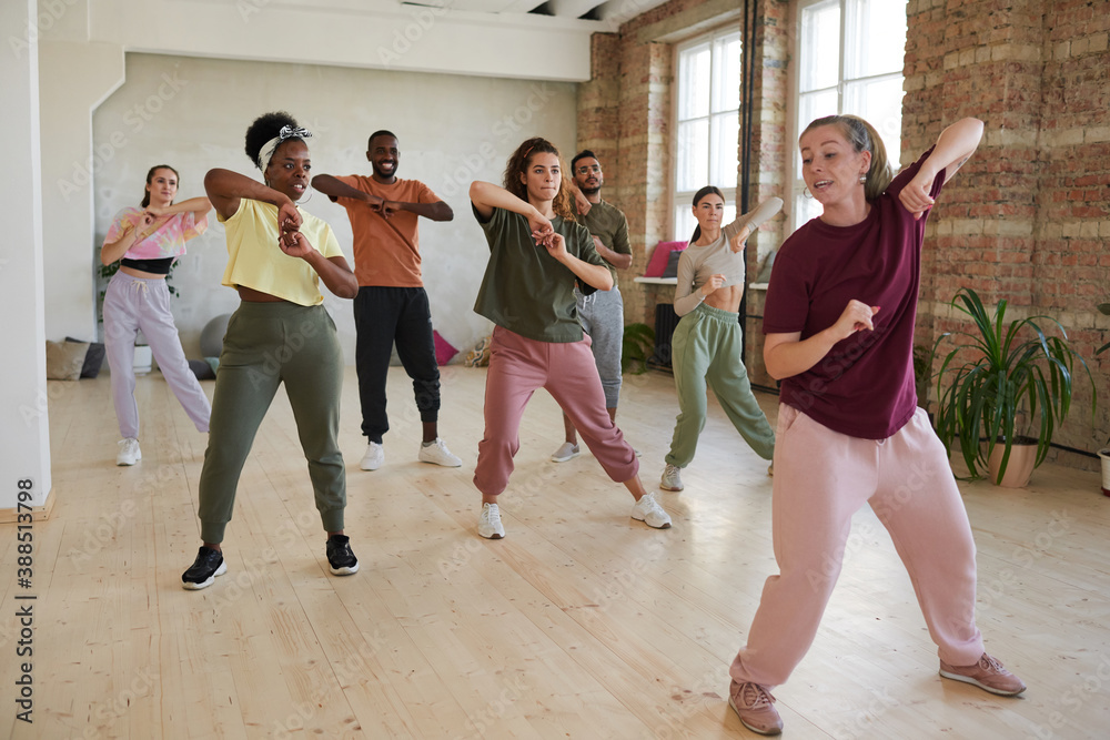 Fototapeta premium Group of people learning dance exercises with instructor in dance hall