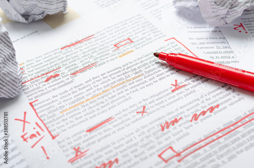 Closeup of text and red marks, crumpled pieces of paper and red marker on the desk.Process of proofreading