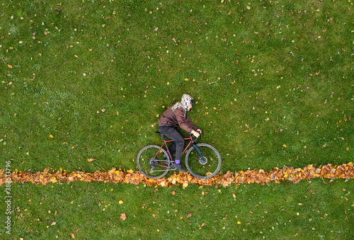 Man with bicycle lies on the green grass with autumn leaves. Creative trendy autumn concept. Drone top view.