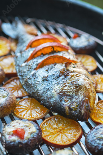 Dorado with oranges and stuffed mushrooms on a charcoal grill. Vertical image.