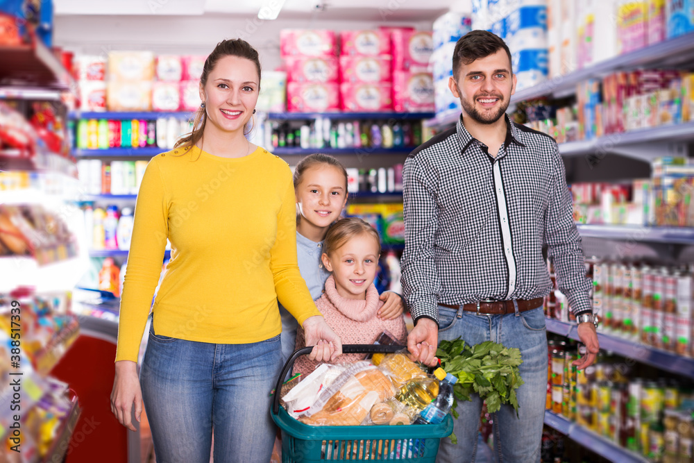 Happy parents with two little girls with purchases during family shopping in grocery store