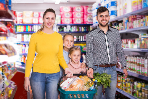 Happy parents with two little girls with purchases during family shopping in grocery store
