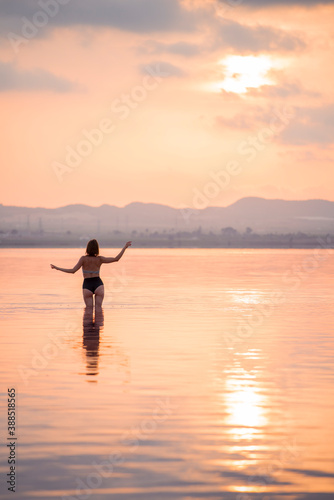 A girl in a bikini stands in the water at sunset. Rear view.