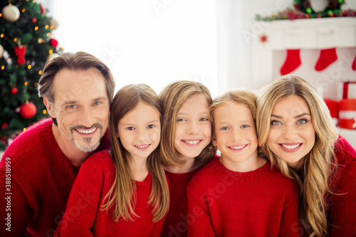 Photo of full family five people gathering three small kids cuddle toothy smiling wear red jumper in decorated living room x-mas preparation evergreen tree lights gift boxes indoors