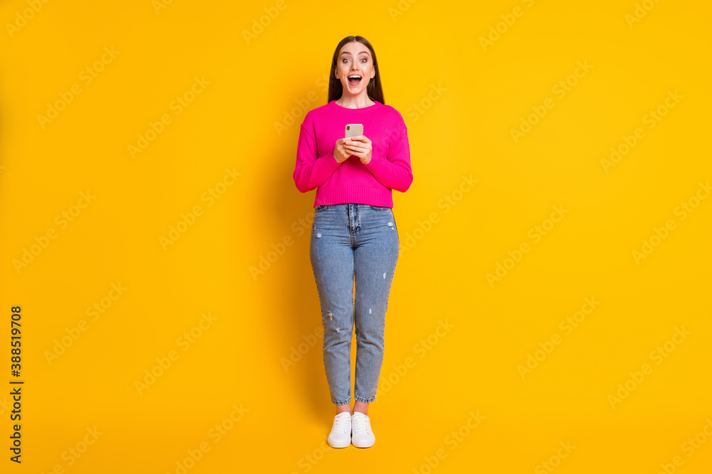 Full length photo of pretty girl hold telephone open mouth wear pink pullover denim jeans sneakers isolated yellow color background Full length photo of pretty girl hold telephone open mouth wear pink pullover denim jeans sneakers isolated yellow color background