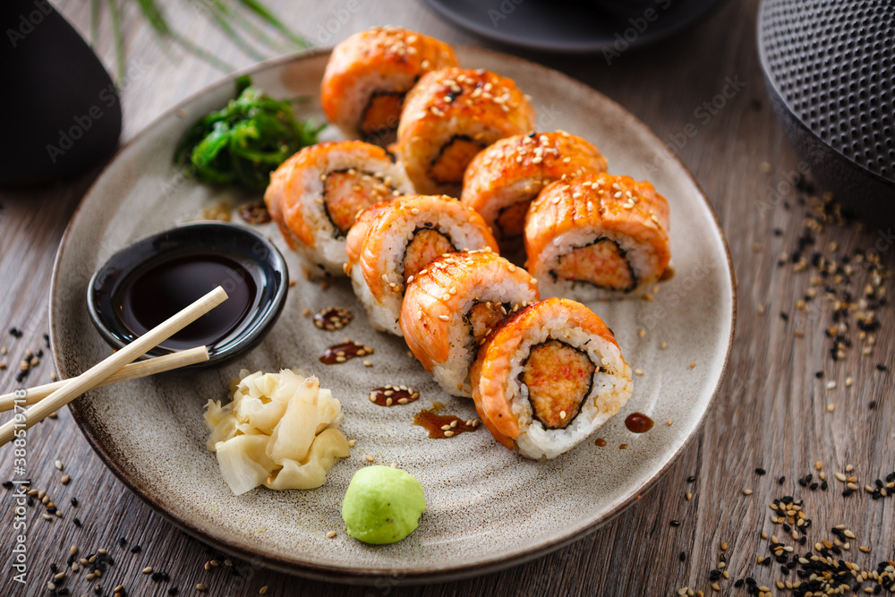 Baked sushi maki rolls with salmon, crab and spicy sauce on a plate with chopsticks, soy sauce, wasabi and ginger. Japanese traditional fish food closeup served for lunch in modern gourmet restaurant Baked sushi maki rolls with salmon, crab and spicy sauce on a plate with chopsticks, soy sauce, wasabi and ginger. Japanese traditional fish food closeup served for lunch in modern gourmet restaurant