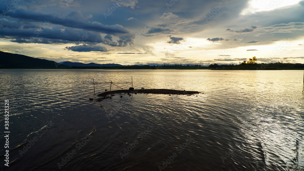 Fototapeta premium The golden sun sets in the evening with a large reservoir and mountains. 
