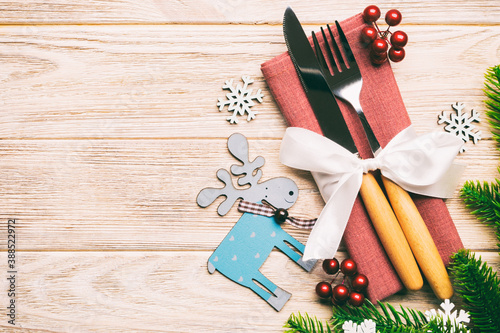 Top view of holiday objects on wooden background. Utensils tied up with ribbon on napkin. Christmas decorations and reindeer with copy space. New year dinner concept