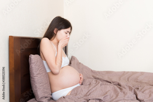 Pregnant suffering with nausea. Pregnancy symptoms, expectation toxicosis. Young vomiting woman sitting on bed. parenthood concept
