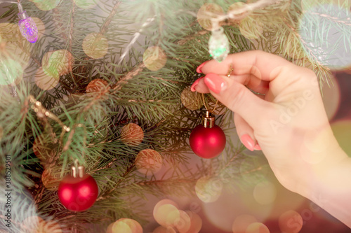 Woman s hand hangs an ornament Christmas ball on a Christmas tree. blurry glow christmas background.
