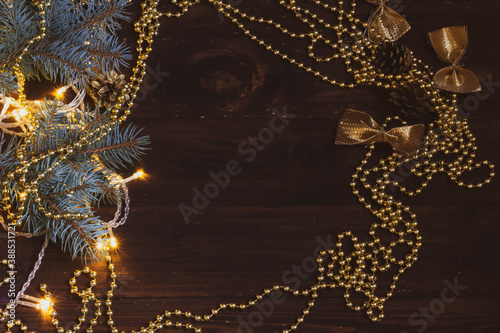 Dark brown wooden background with Christmas decorations: Golden cones, Golden ribbons, blue-green spruce with long beautiful needles. Gold beads create a frame and free space for text.