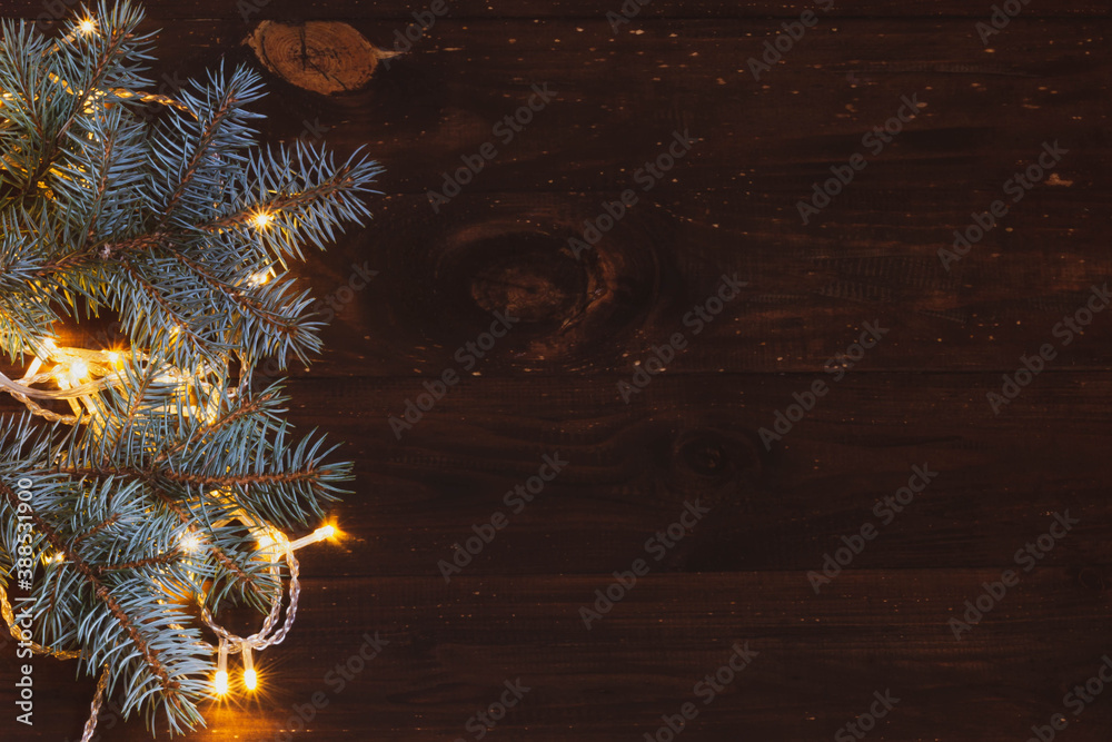 Christmas background of glowing ice yellow garland and branches of a beautiful Christmas tree on a brown dark wooden background. Natural background for the Christmas holiday. copy space. Christmas background of glowing ice yellow garland and branches of a beautiful Christmas tree on a brown dark wooden background. Natural background for the Christmas holiday. copy space.