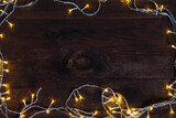 Christmas background of led garlands of warm white light on a wooden surface made of dark brown textured boards. Frame of glowing light bulbs, copy space.
