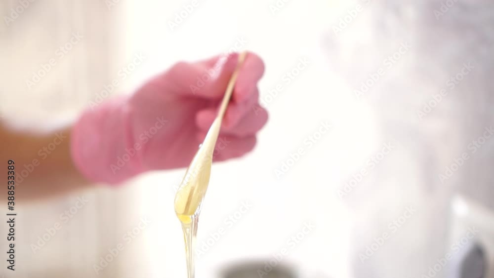 Sugar paste in a white jar on a pink background.A master in pink gloves stir the sugar paste before removing unwanted hair.Sugaring.Depilation. Epilation.Beauty concept.Selective focus on sugar paste. Sugar paste in a white jar on a pink background.A master in pink gloves stir the sugar paste before removing unwanted hair.Sugaring.Depilation. Epilation.Beauty concept.Selective focus on sugar paste.