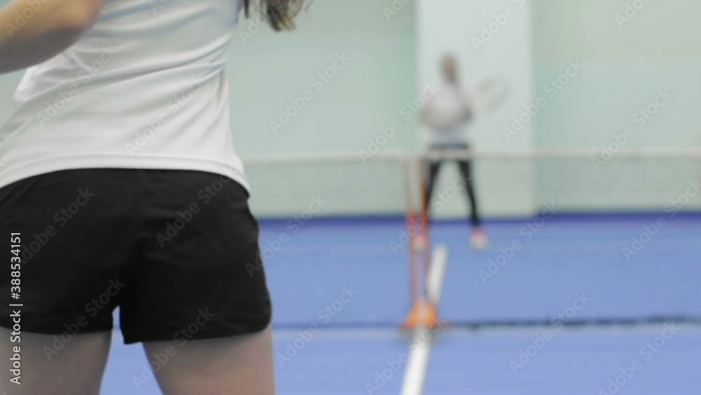 A young woman in a white t-shirt and black shorts plays tennis in the gym. The view from the back. A young woman in a white t-shirt and black shorts plays tennis in the gym. The view from the back.