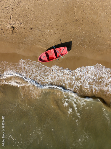 Aerial top down view of red fishing boat anchored on sand beach near sea waves. Nautical vessel, water transport. Minimalism art nature photography.