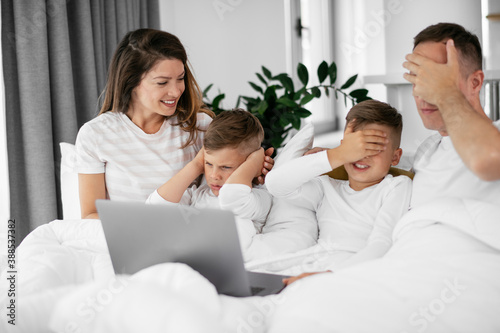 Beautiful parents with kids enjoying at home. Young family watching movie on lap top..