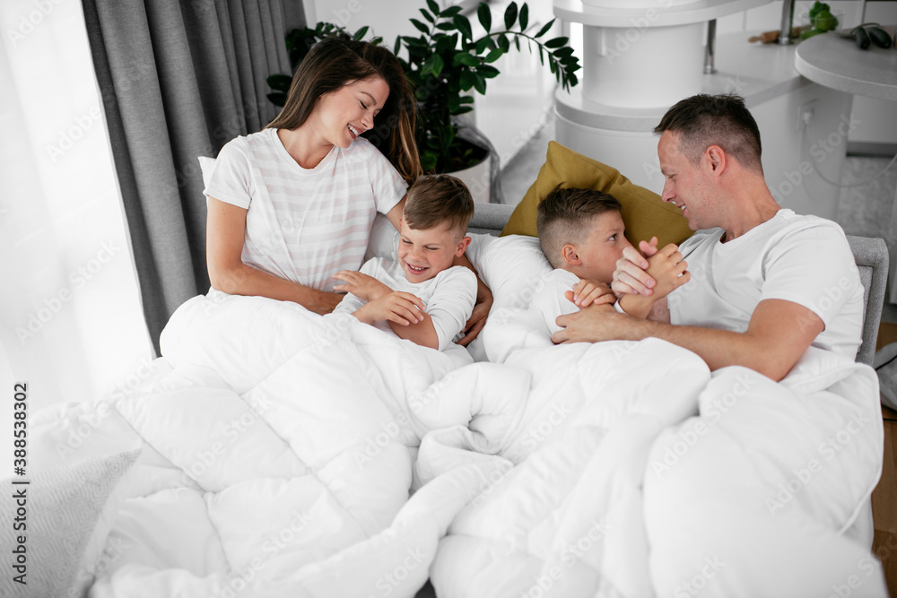 Young family enjoying in bed. Happy parents with sons relaxing in bed. Young family enjoying in bed. Happy parents with sons relaxing in bed.