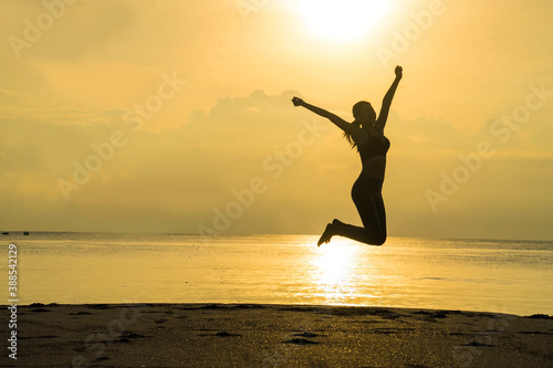 Silhouette of Asian girls jumping with arms raised to feel free and enjoying life on the beach at sunrise in morning .Freedom and Wellbeing concept.