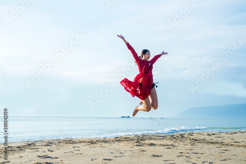 Asian girls jumping with arms raised to feel free and enjoying life on the beach at sunrise in morning .Freedom and Wellbeing concept.
