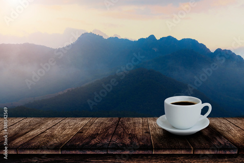 White cup of hot coffee on wooden table with mountain fog background