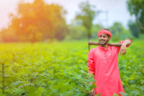 Young indian farmer holding farm equipment in hand at cotton fie photo