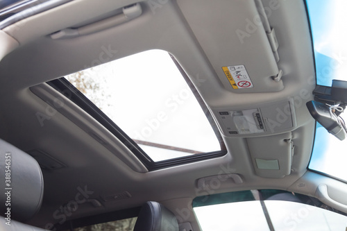 View of the ceiling of the car with a transparent glass hatch for airing, opening in summer while driving fast in the gray cabin of the vehicle. Sunroof on light coloured beige roof.