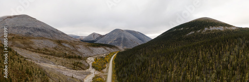 Panoramic View of Scenic Road from Above surrounded by Mountains and Forest on a Cloudy Fall Day. Aerial Drone Shot. Taken near the Dempster Highway, Yukon, Canada.