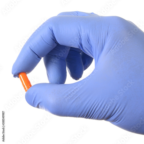 Hand in latex medical glove holding capsule drugs