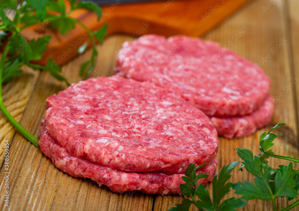 Raw meat cutlets with parsley on wooden cutting board