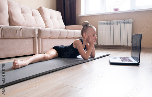 The child watches online video on a laptop and performs sports exercises - yoga, gymnastics. Stay at home. Self-isolation, quarantine, online education concept.