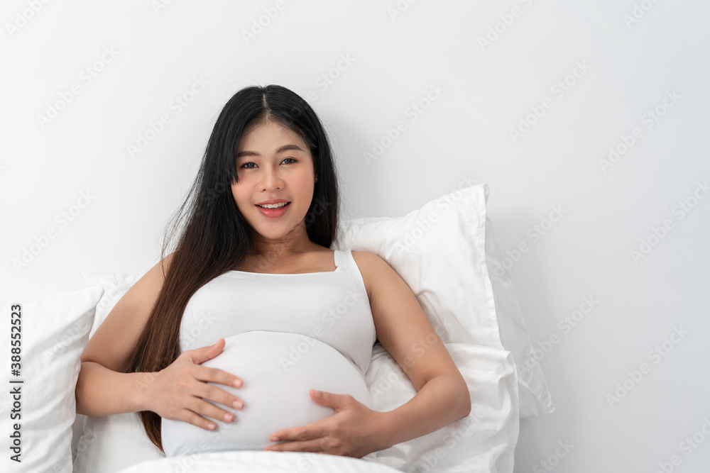 Asia happy pregnant woman is sitting on bed and and touching her belly. pregnancy, motherhood, people and expectation concept Asia happy pregnant woman is sitting on bed and and touching her belly. pregnancy, motherhood, people and expectation concept