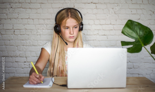 Teenage girl in headphones studying online and making notes in notebook, e-learing and homeschooling concept. photo
