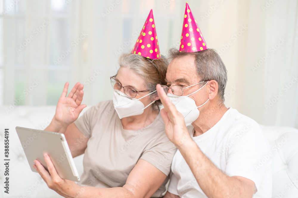 Senior couple wearing party's caps and protective masks celebrates  birthday with her family on video call during the coronavirus epidemic